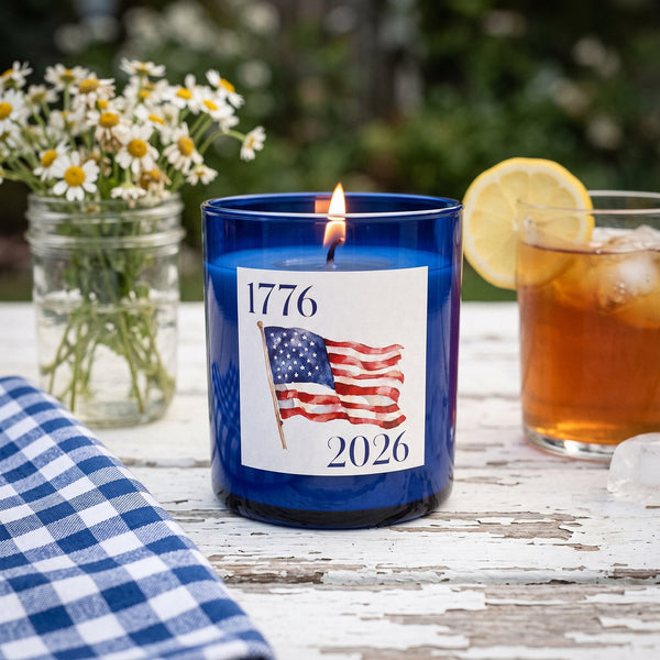 1776-2026 Candle burning on a weathered white picnic table on a summer evening | Noteology
