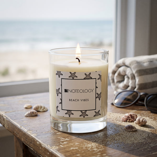 Beach Vibes Candle burning on a beach house table by a window, with a blurred ocean and bright daylight outside | Noteology