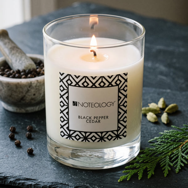 Black Pepper Cedar Candle burning on a dark slate surface in soft side light | Noteology