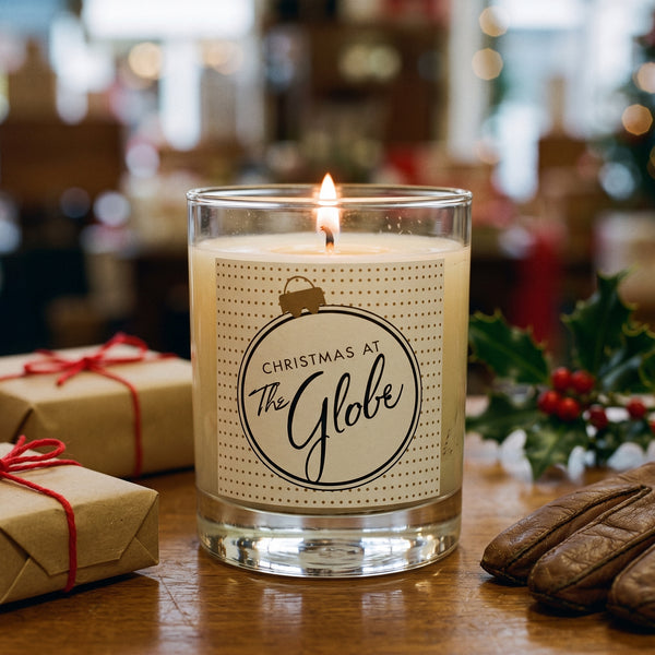 Christmas at the Globe Candle burning on a polished wooden shop counter in warm holiday light | Noteology