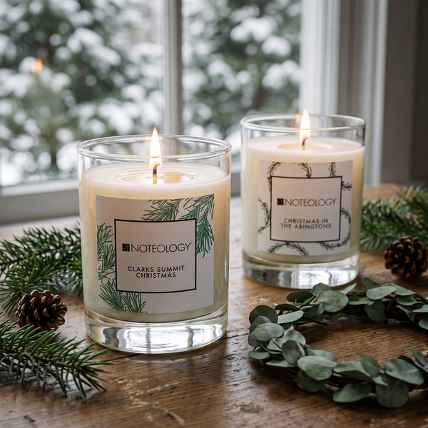 Clarks Summit Candle Duo burning on a wooden farmhouse table by a window with snowy pines outside | Noteology