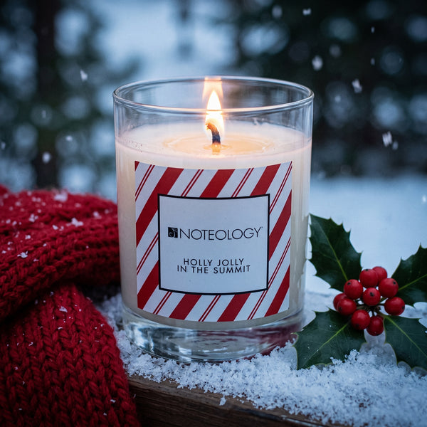Holly Jolly in the Summit Candle burning on a snow-covered porch railing at blue dusk | Noteology