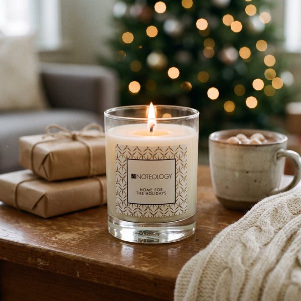 Home for the Holidays Candle burning on a living-room side table beside a Christmas tree with warm lights | Noteology
