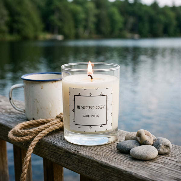 Lake Vibes Candle burning on a wooden dock railing | Noteology