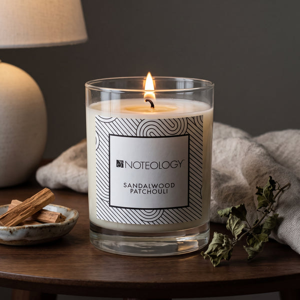 Sandalwood Patchouli Candle burning on a dark wood side table in a calm, dim living room | Noteology