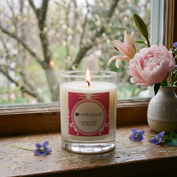 Scranton In Bloom Candle burning on a windowsill in spring, with blurred budding trees outside | Noteology