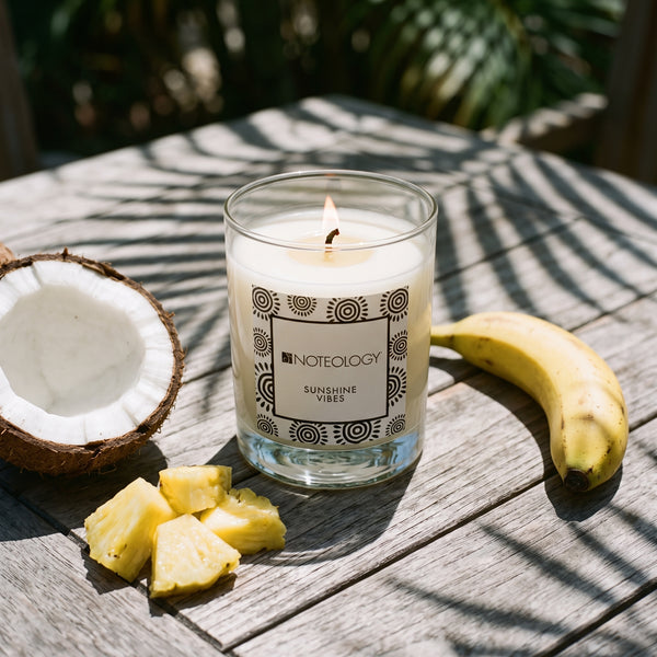Sunshine Vibes Candle burning on an outdoor table in bright tropical sun with palm-leaf shadows | Noteology