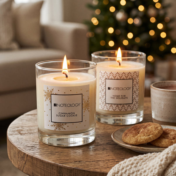Warm & Cozy Candle Duo burning on a living-room side table beside a Christmas tree with warm lights | Noteology